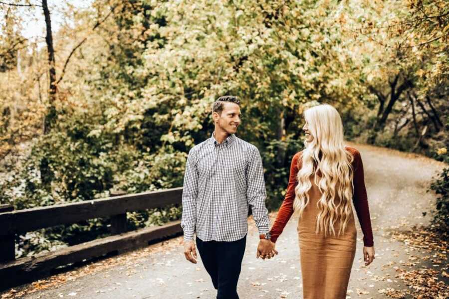 Couple walk hand-in-hand over a nature bridge during romantic fall-themed photoshoot