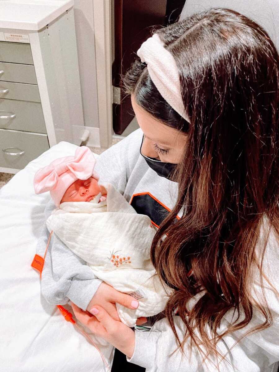 First time mom holds her newborn premature daughter while wearing a face mask