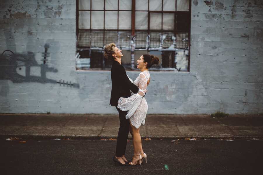 Newly married LGBTQ couple pose for a photo, one in a white dress and one in a black pantsuit