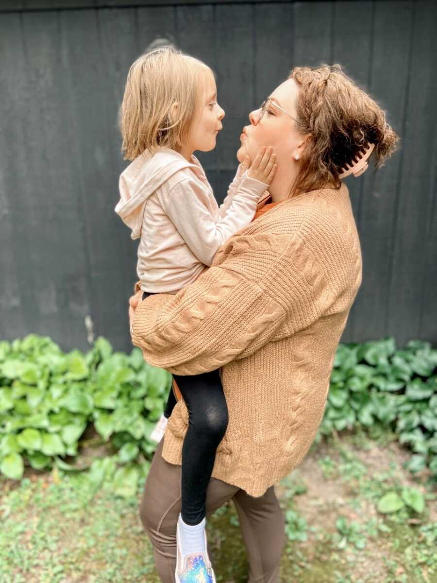 Mom and daughter make kissy faces at each other while taking photos together before school