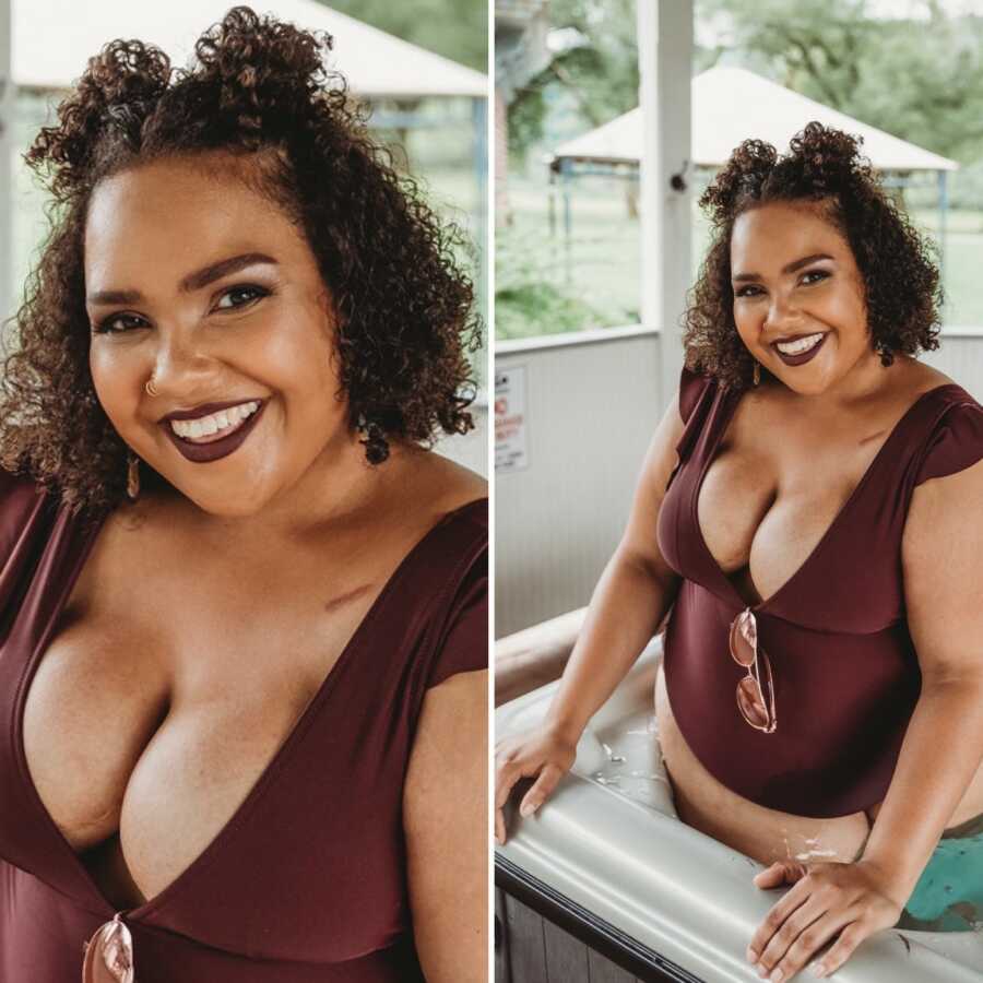 Cancer survivor smiles in a dark plum bathing suit and matching lipstick while showing off her port scar from chemotherapy