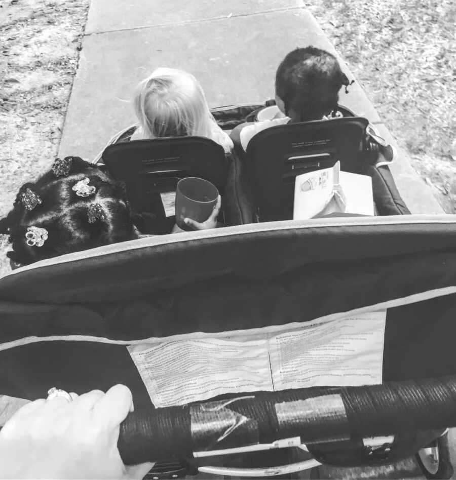 Foster mom pushes a baby stroller down the sidewalk with three children sitting in it