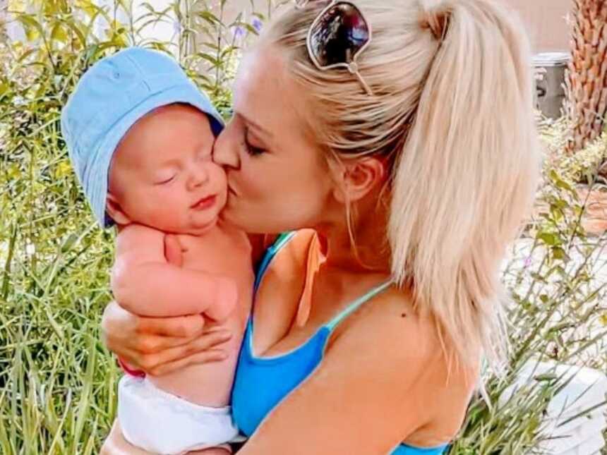 Mom kisses her newborn son on the cheek while enjoying the summer weather together