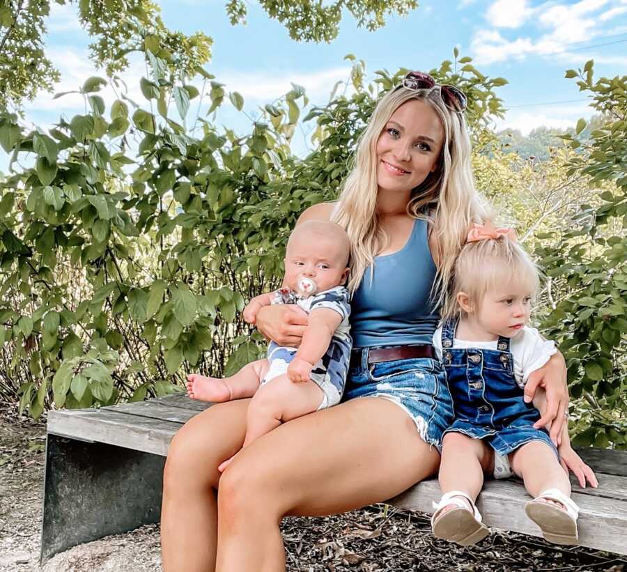 Mom poses with two of her three children while out on a walk wearing a blue tank top and jean shorts