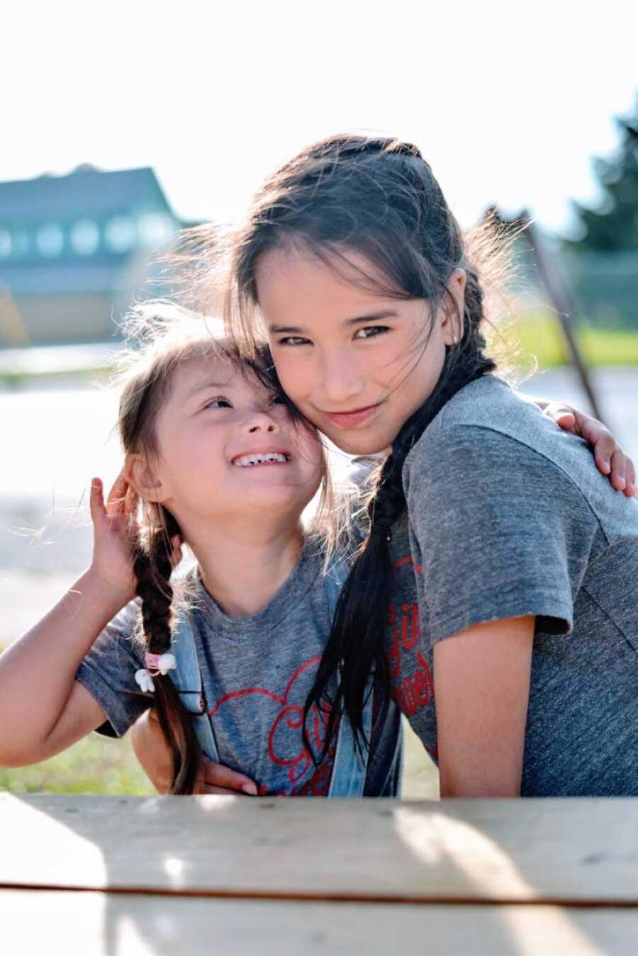 Two sisters wearing matching shirts with matching braids smile for a photo together