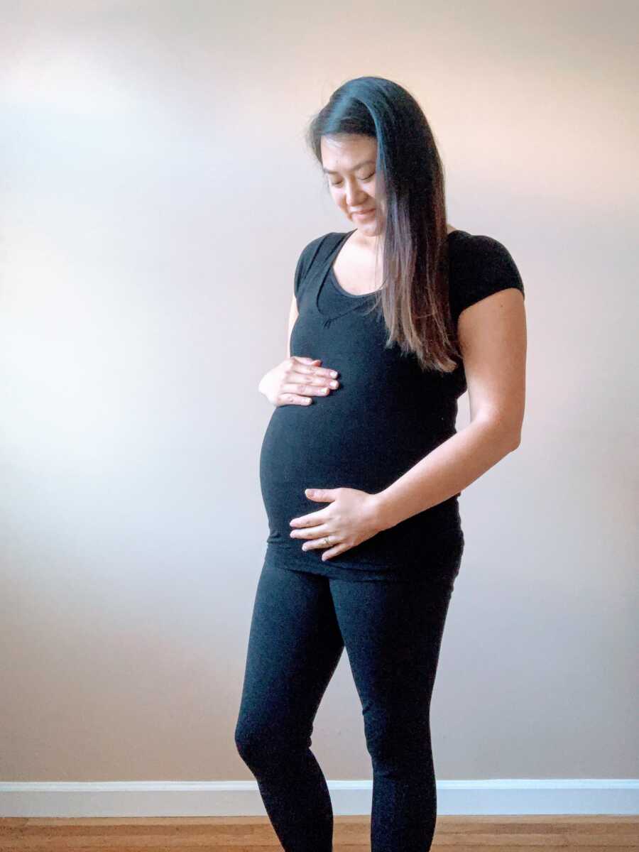 Korean adoptee smiles down at her belly in an all-black outfit during her first pregnancy