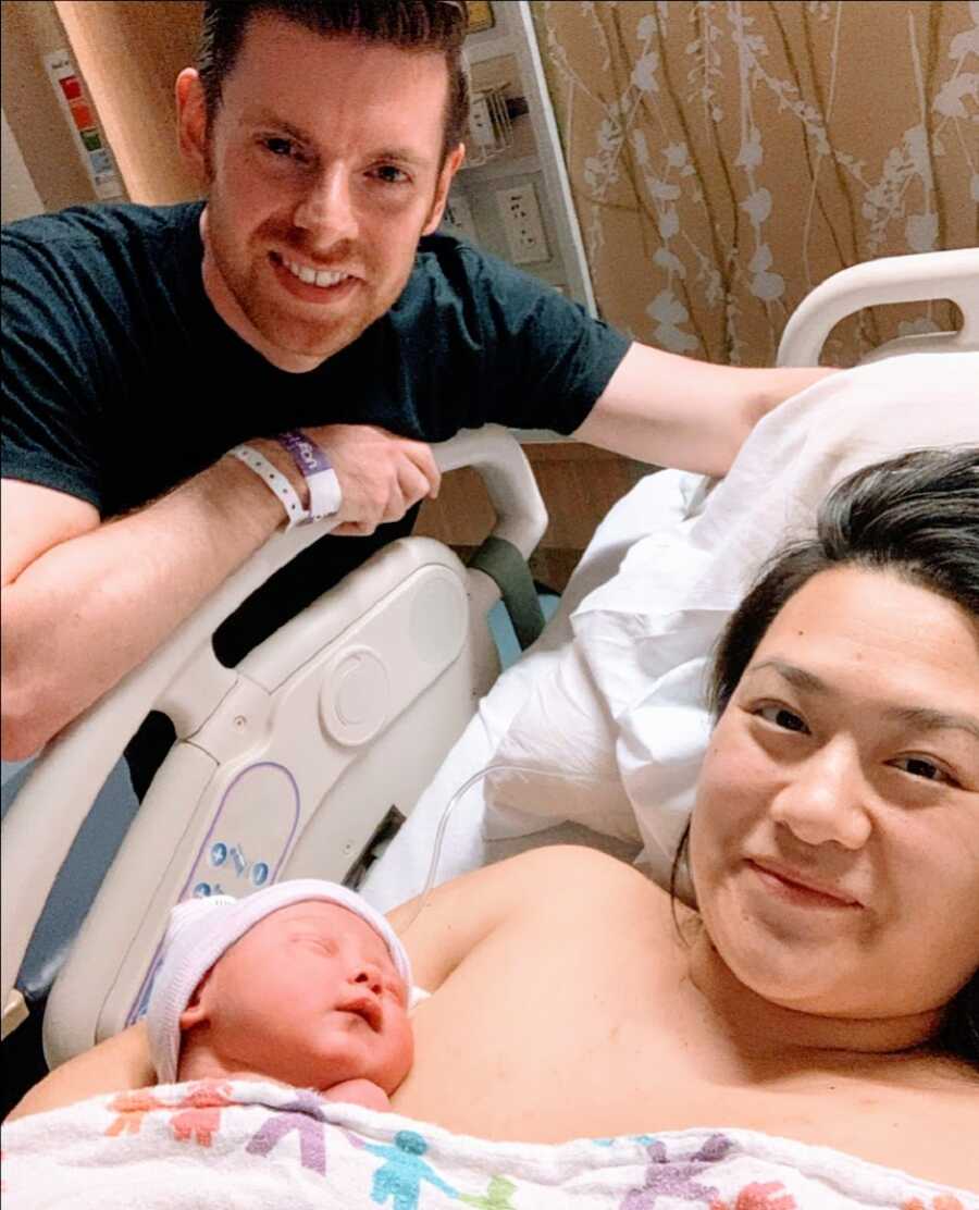 New parents take a hospital selfie with their newborn daughter, showing off their joy