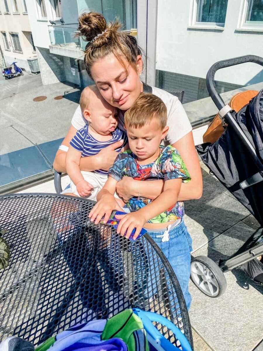 Mom hugs her two sons while sitting outside at a restaurant while on vacation in Switzerland