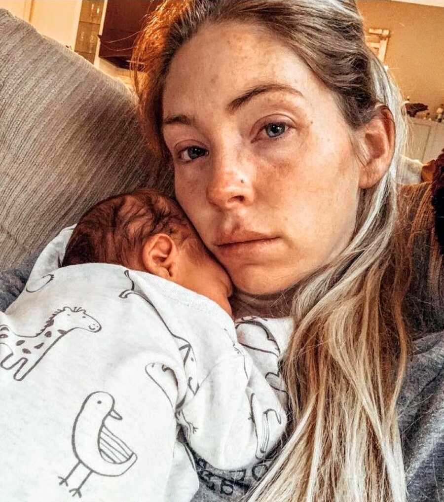 Mom battling postpartum anxiety holds her newborn while fighting back tears