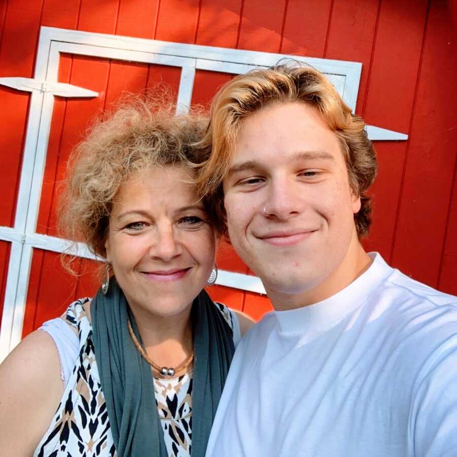 Mom takes a selfie with her youngest son in college in front of a red barn