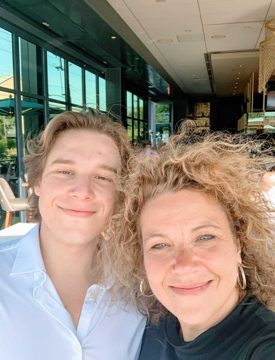 Mom with crazy curly hair takes a selfie with her son while visiting him at college