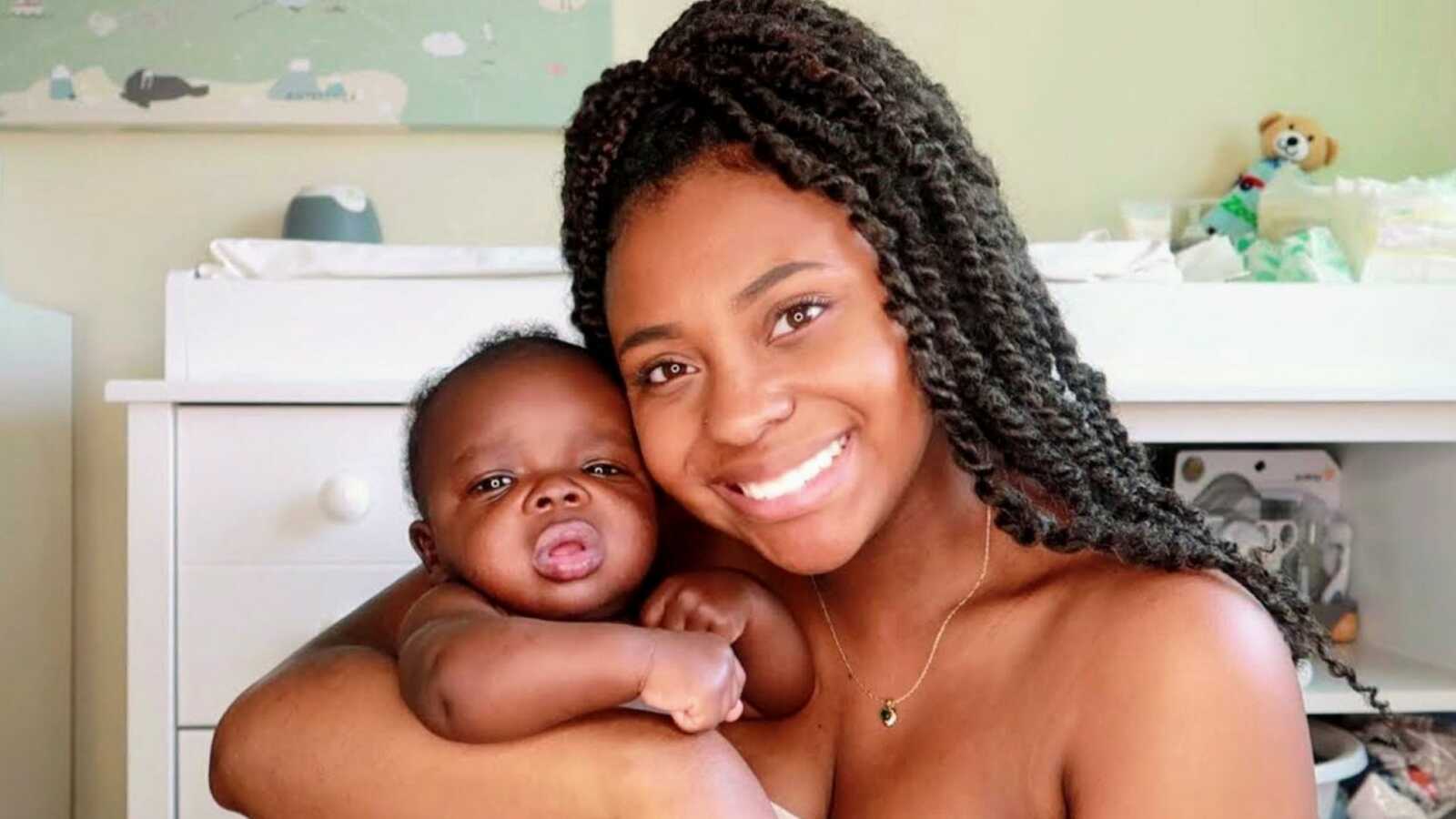 Young single mom takes a photo with her newborn son while they spend quality time together in his nursery