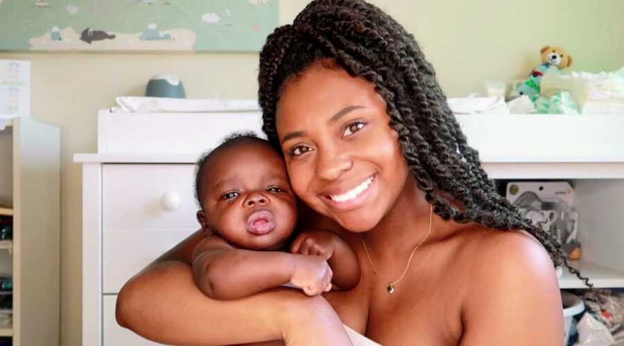 New mom holds her newborn son while they take a photo together in his nursery