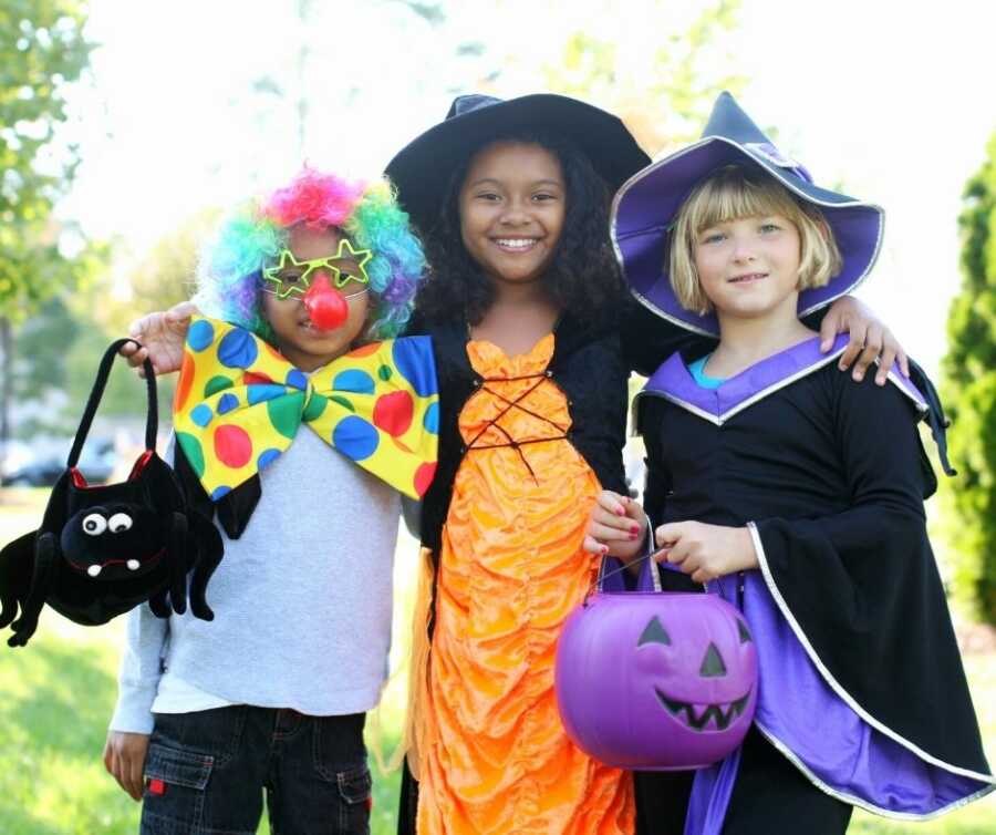 Three kids dressed in Halloween costumes get ready to trick-or-treat.