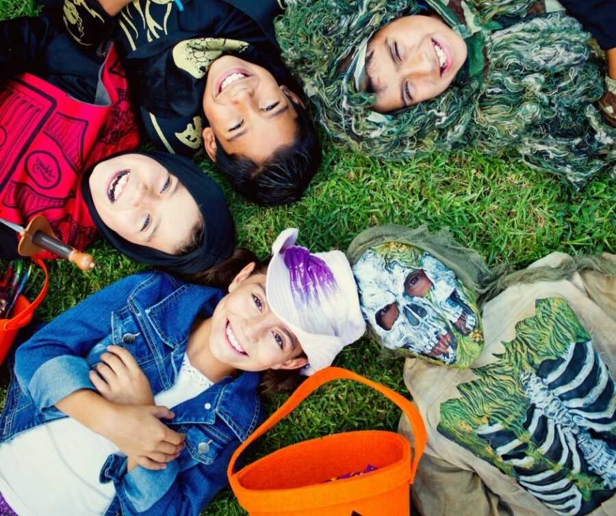 Children in Halloween costumes lay in a circle and smile up at the camera.