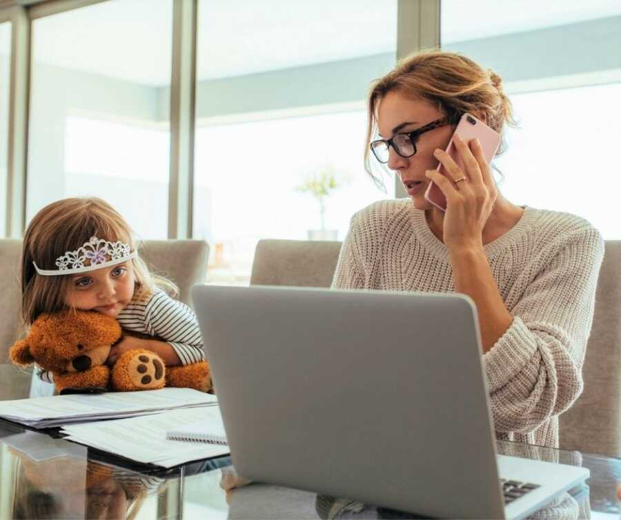 Little girl with tiara and teddy bear watches busy working mom.