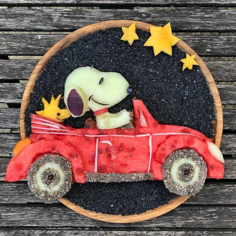 Edible food art fruit platter scene of Snoopy and Woodstock in a red car.