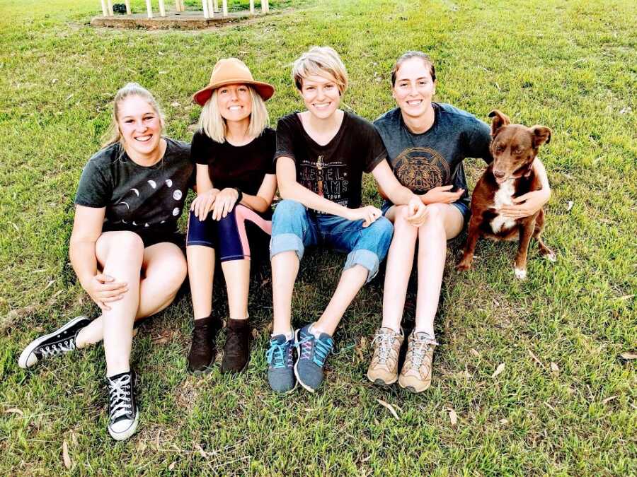 Woman and friends sit with dog on the grass