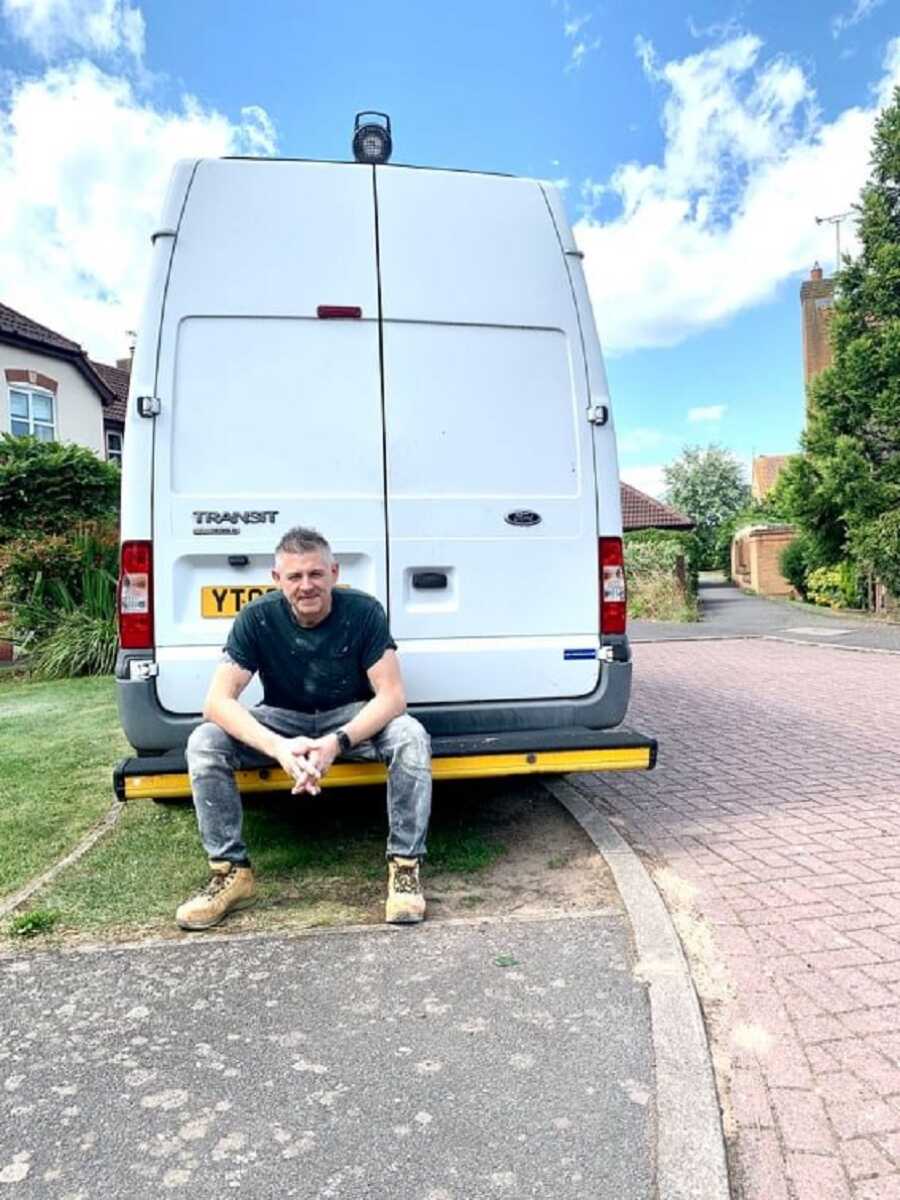 Plumber sits on the bumper of his work van, posing for the camera.