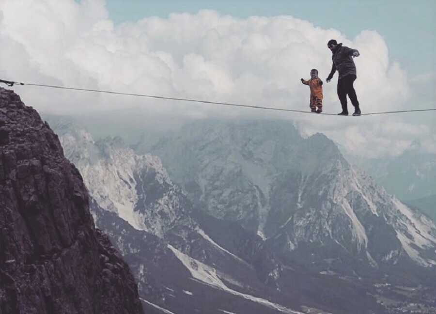 Dad and baby walk tight rope over mountain plunge.