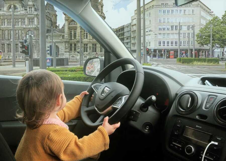 Toddler appears to be driving the car through city streets. 