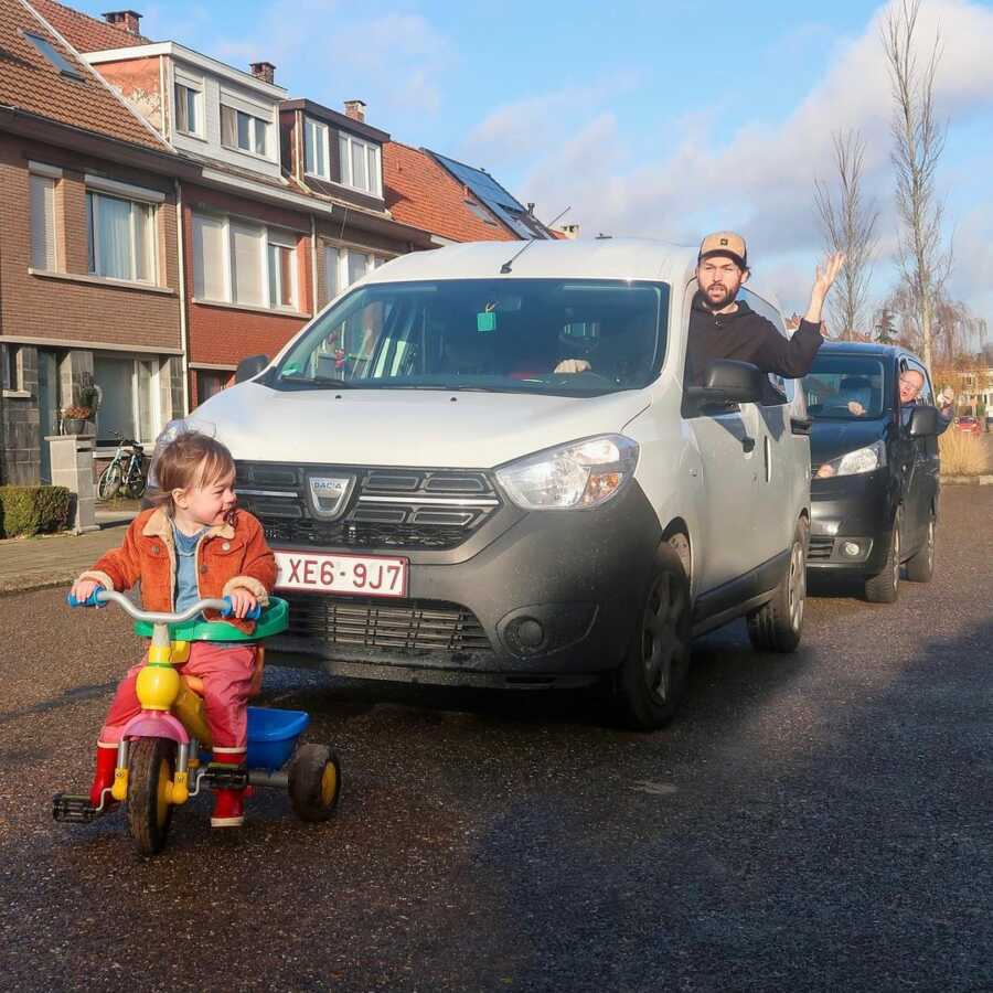 Cars line up in traffic jam behind a toddler on a plastic tricycle.