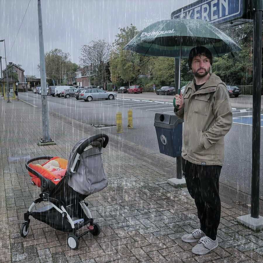 Dad takes picture in the rain, appearing to have remembered his own umbrella but not one for the baby.