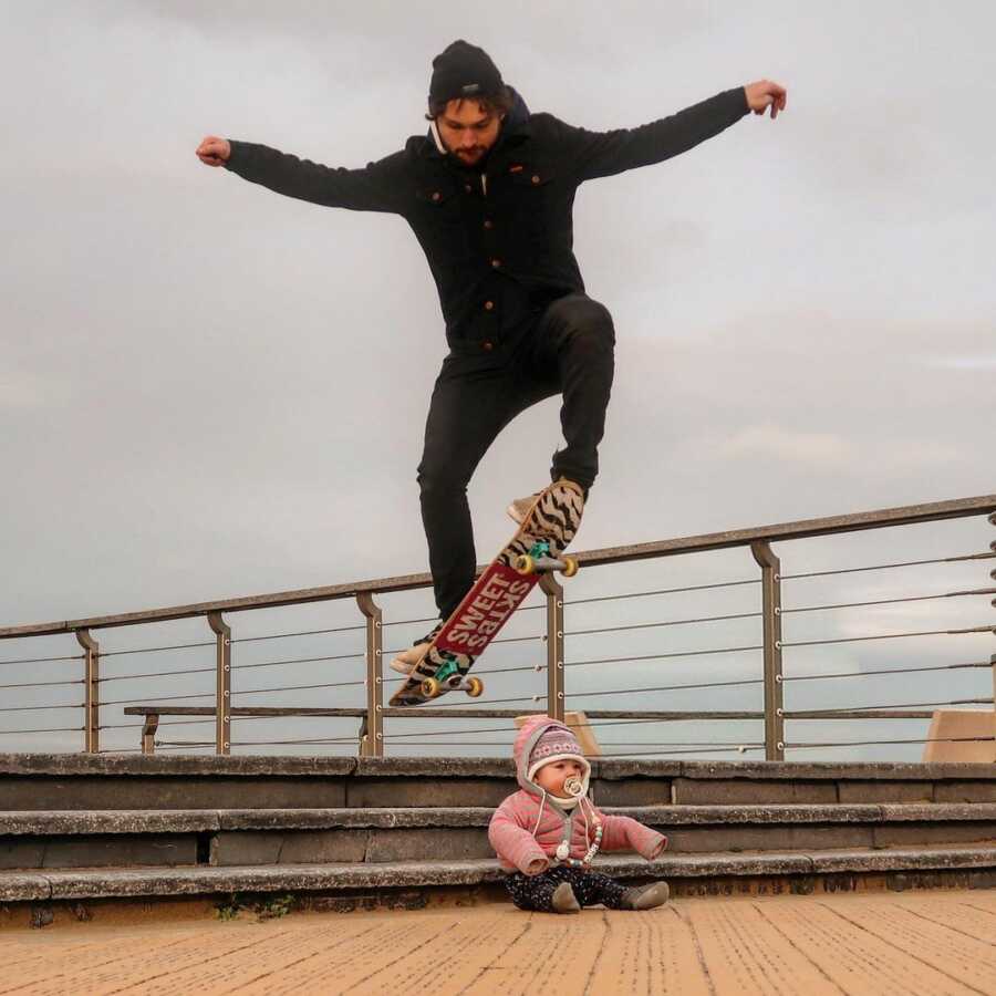 Dad creates picture performing skate board trick jumping over baby. 