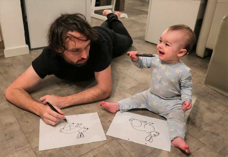 Dad looks at baby's drawing of a rabbit, which is much better than his. 