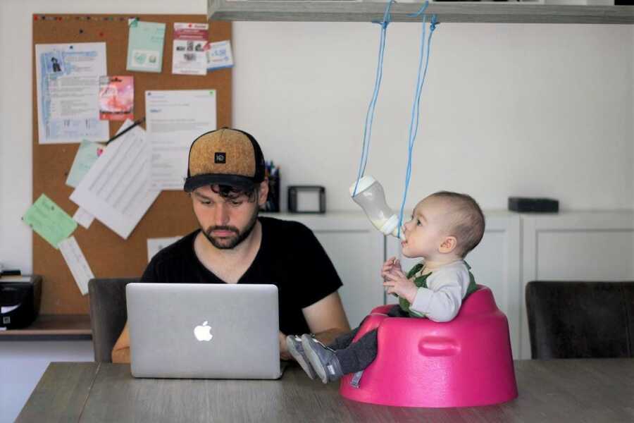 Dad suspends baby's bottle so they can feed themselves while he works. 