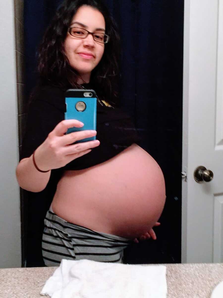 Pregnant woman with belly exposed holds phone