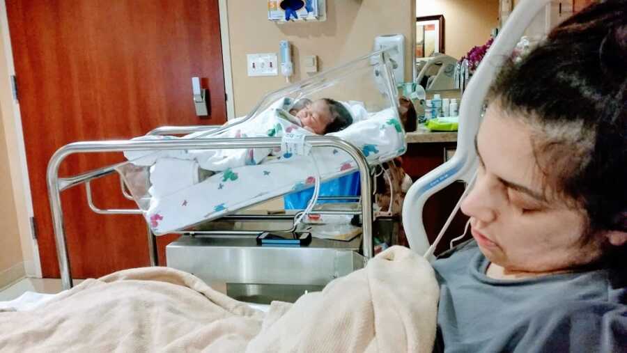 Mother lying in hospital bed with baby in bin