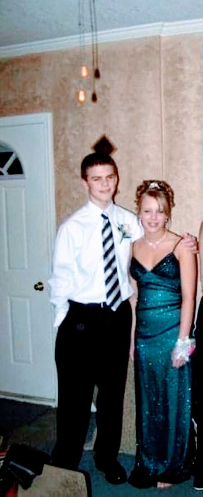 Teen couple in love take a photo together before Prom, girl in a sparkly emerald dress with her hair up and boy in a suit with a matching tie