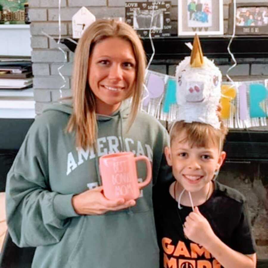 Bonus mom takes a photo with her bonus son at her birthday party while she holds a pink mug that says "Best Bonus Mom"