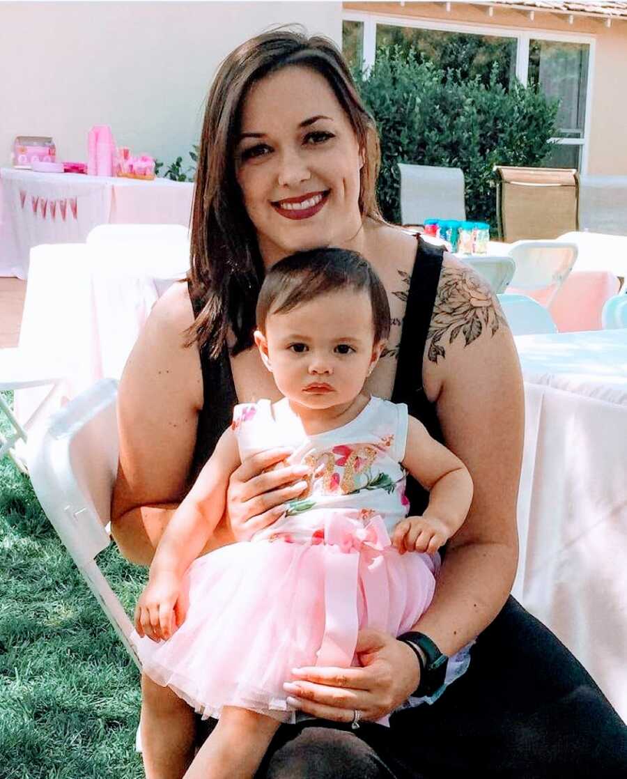 Girl mom holds her one-year-old daughter at her princess pink themed birthday party
