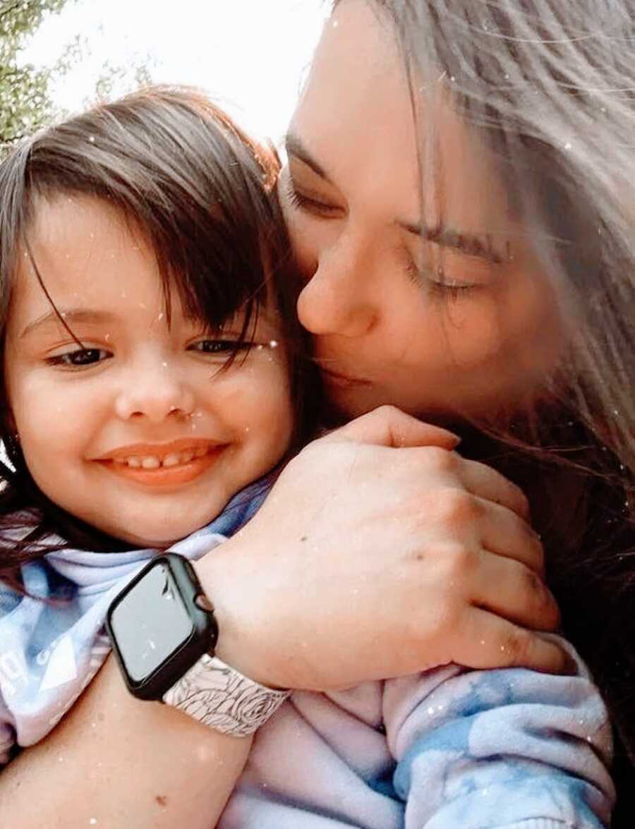 Mom kisses her daughter on the cheek and hugs her while they take a selfie together