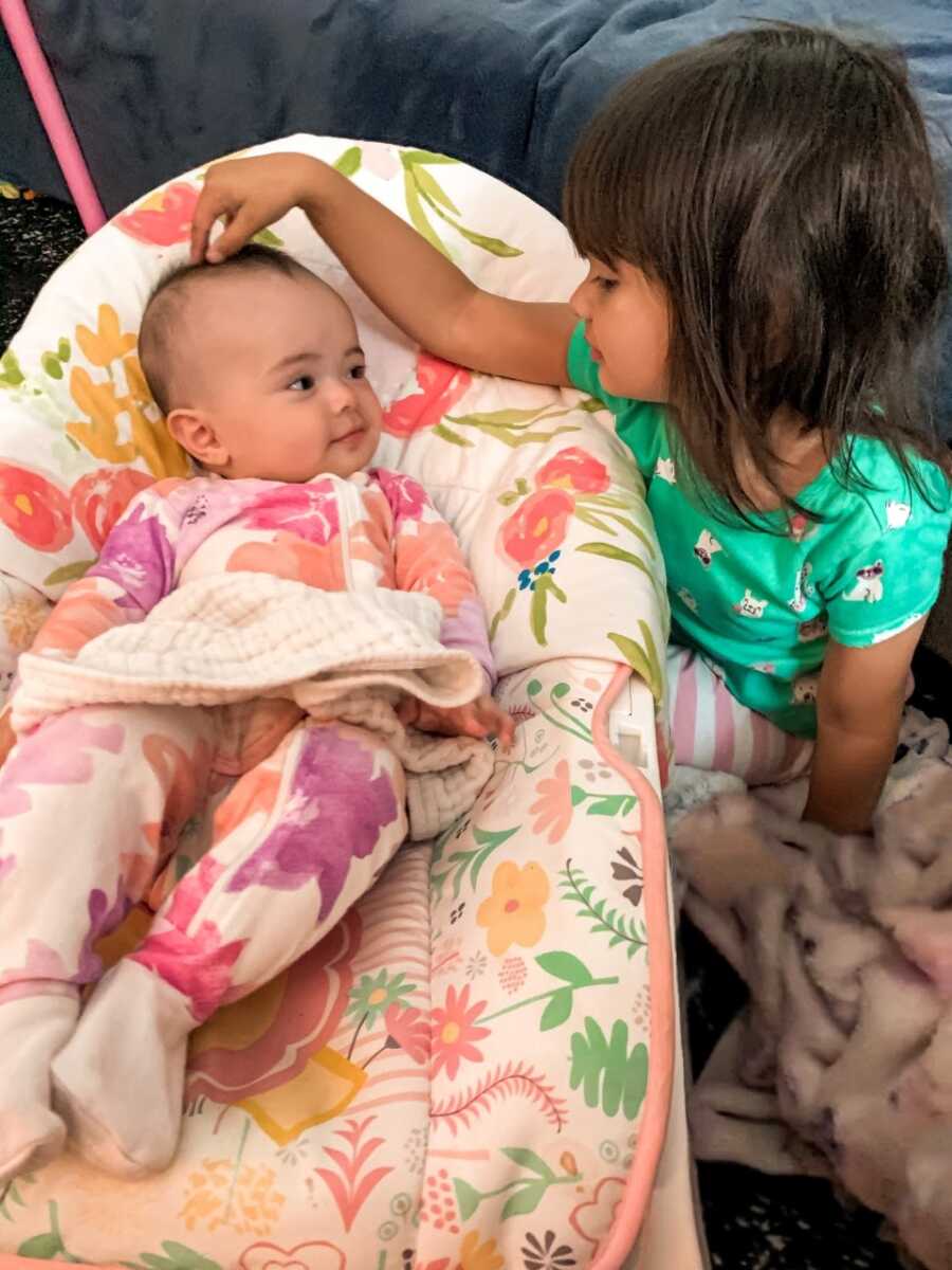 Little girl with autism watches her baby sister laying in a bassinet