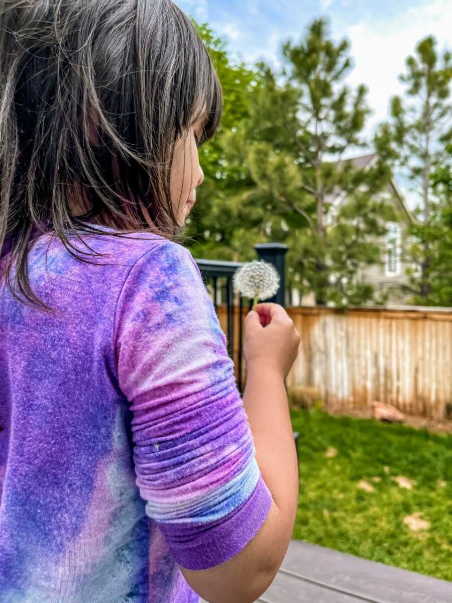 Little girl with autism wishes on a dandelion before blowing it away in her backyard