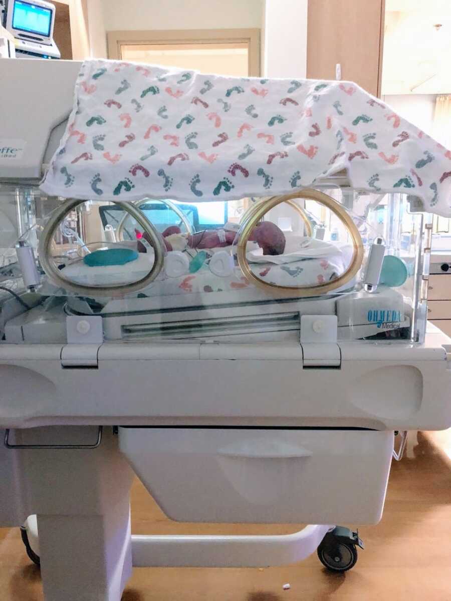 Mom snaps a photo of her third child sleeping in an isolette in the NICU