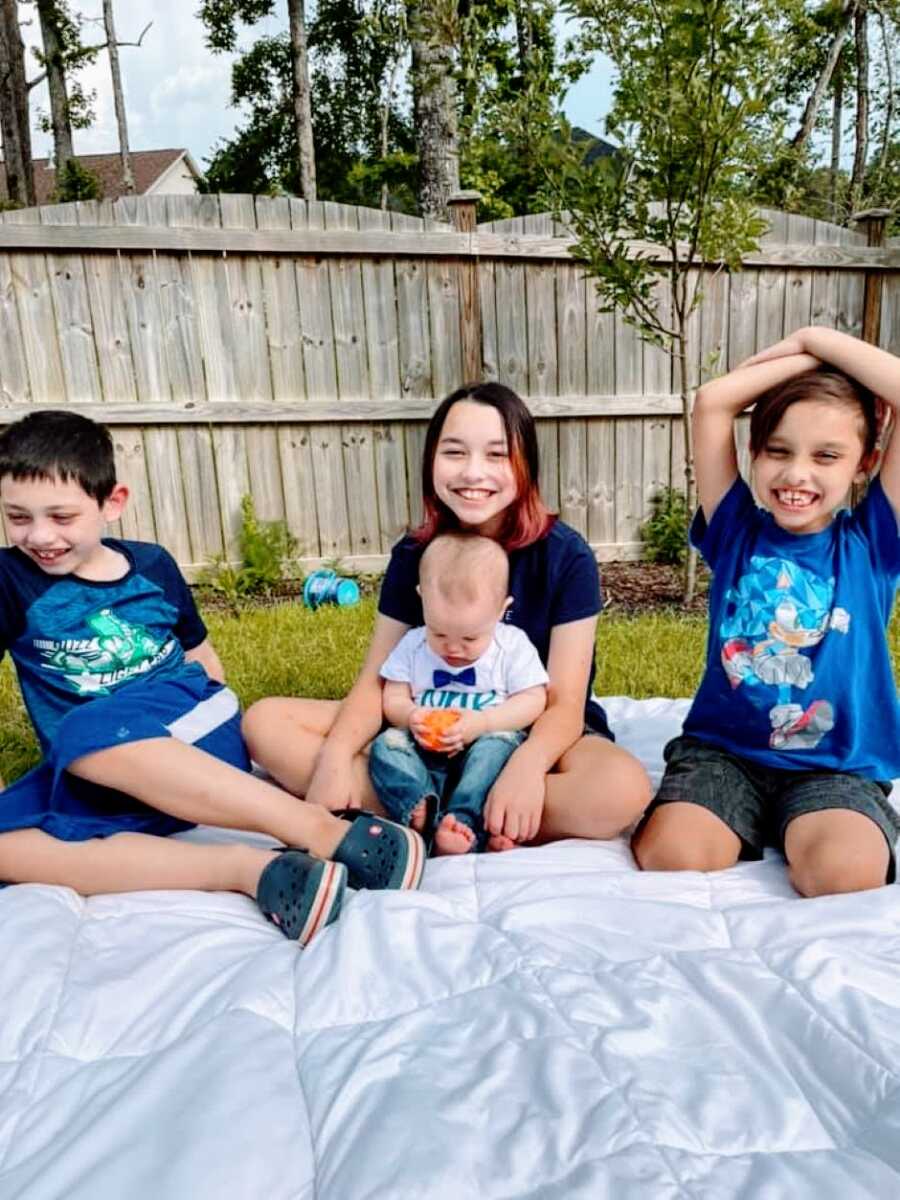 Mom snaps a photo of her four kids hanging out in the backyard on a blanket