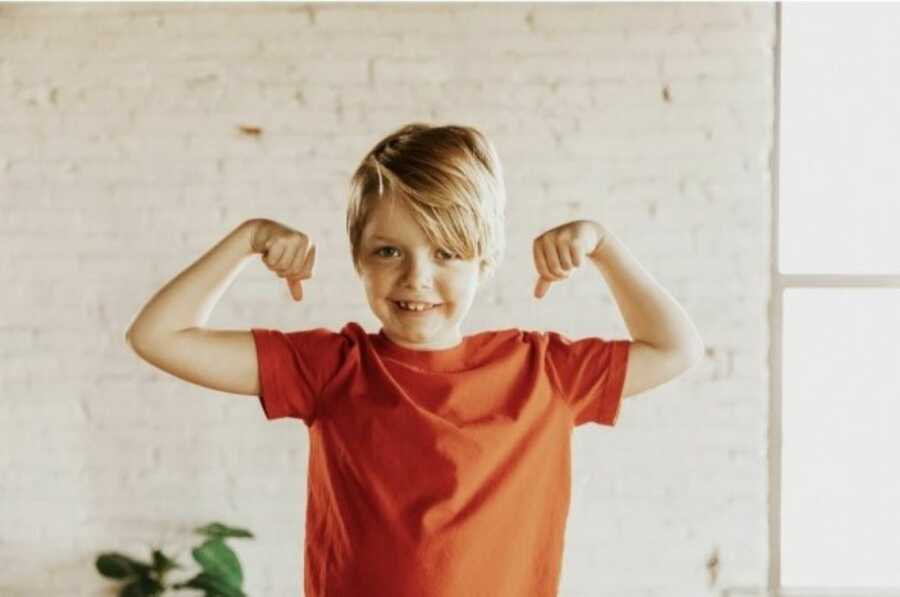 Little boy adopted by his parents poses for a photo, smiling big while showing off his muscles