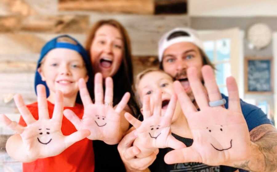 Family of four take a photo together with smiley faces drawn onto their hands