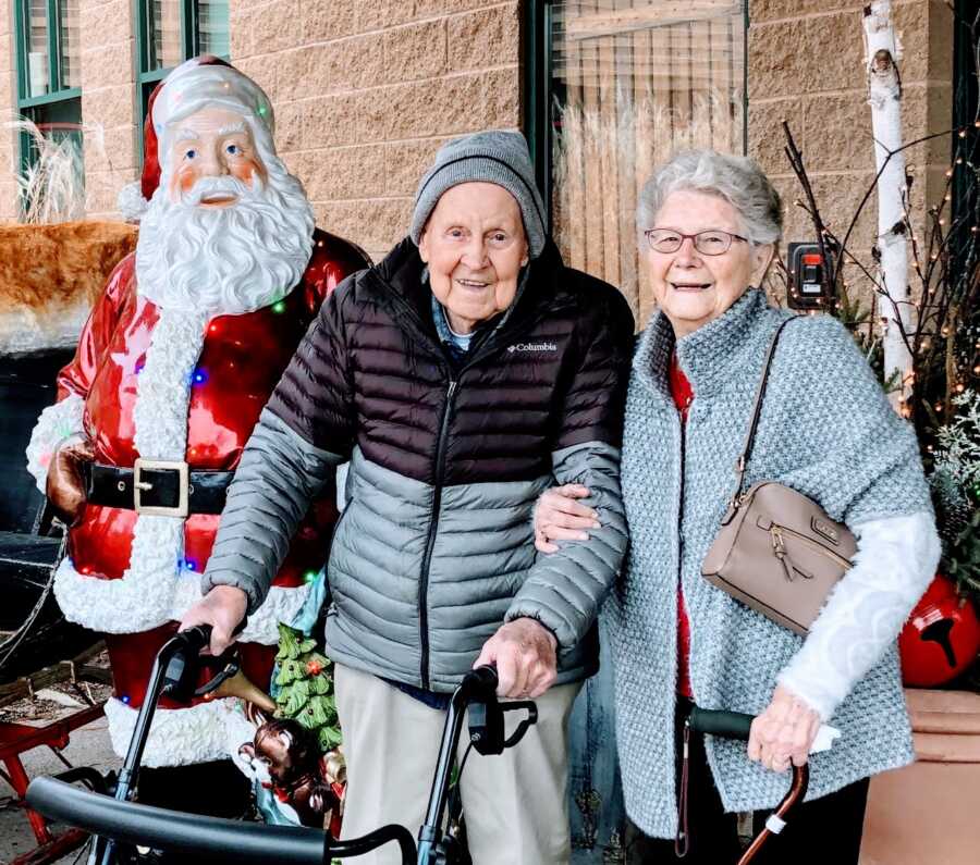Elderly couple pose together during Christmas time next to a light-up Santa statue