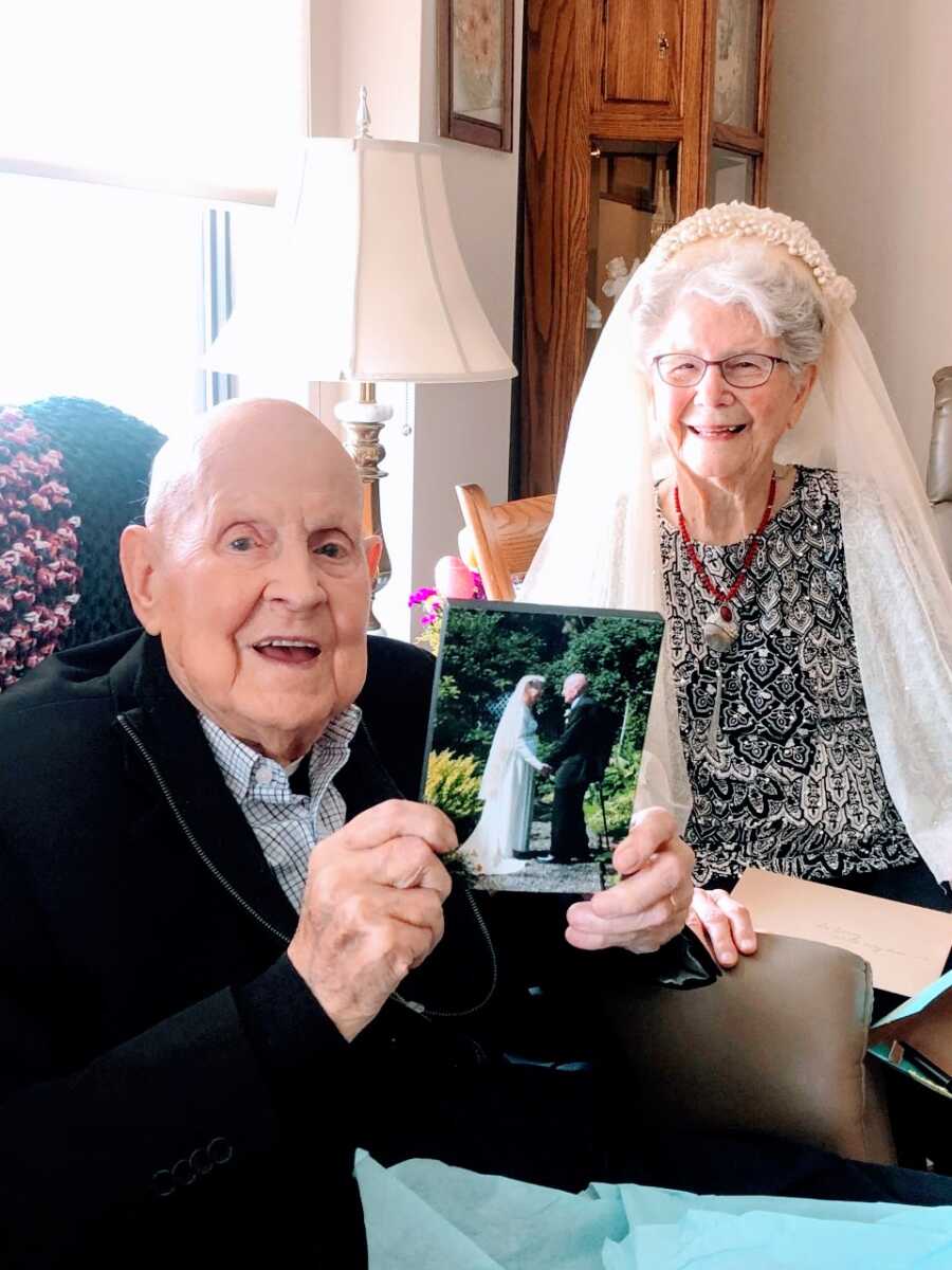 一对老夫妇在他们的75周年结婚纪念日上笑容灿烂，而丈夫则拿着他们重新宣誓时的照片
