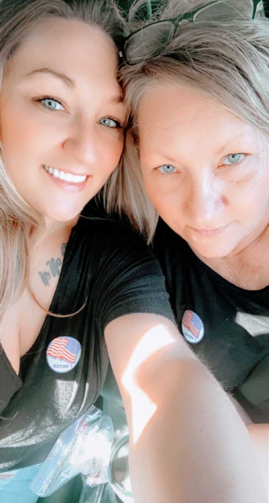 Young woman takes a selfie with her mom while they both wear black t-shirts and "I voted" stickers