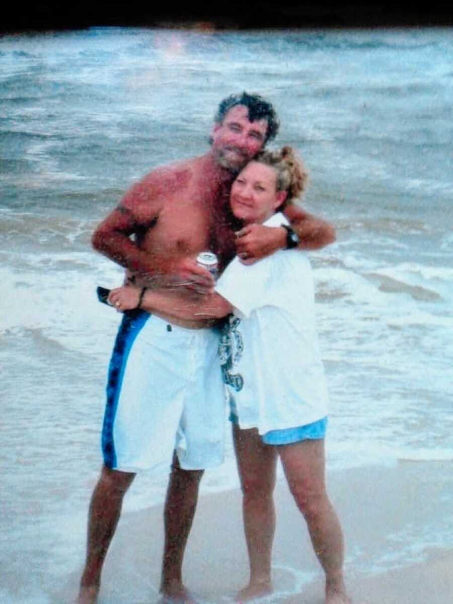 Woman shares an old photo of her mom and stepdad hugging for a photo while enjoying time together at the beach