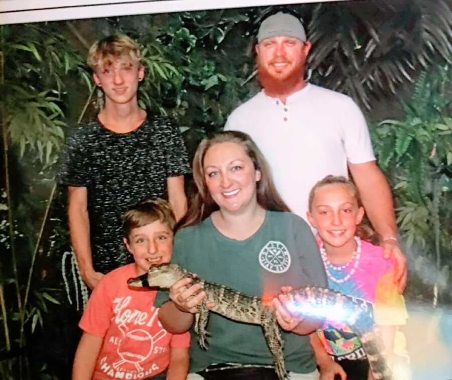 Blended family of five take a photo together while the mom holds a baby alligator with its mouth taped shut