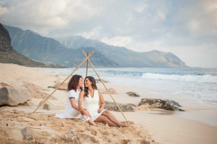Newlyweds take photos together out on the beach, both wearing white