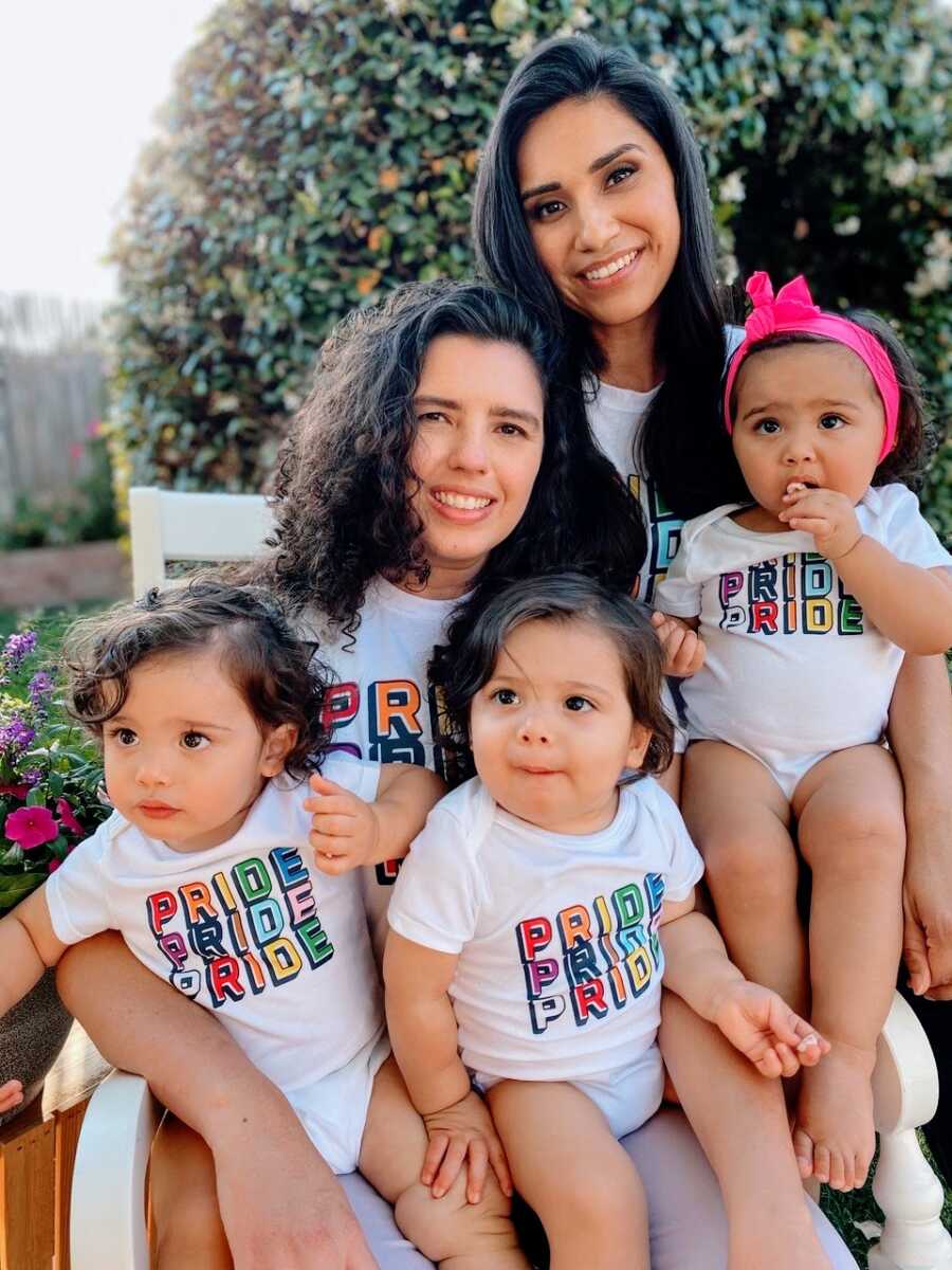 Two mom take a family photo with their toddler triplets, all wearing matching "Pride" shirts during Pride month
