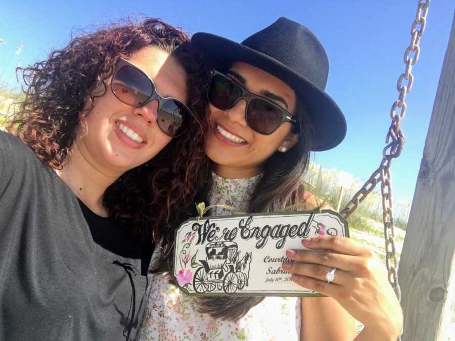 Lesbian couple announce their engagement with a sign that reads "We're engaged" with the date